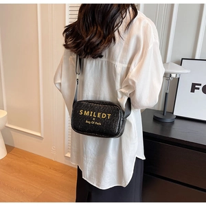 Detail of black pebbled leather crossbody bag with adjustable strap and gold logo lettering