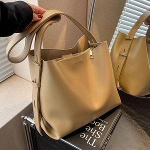 Minimalist khaki matte leather bucket bag with wide strap and gold hardware on mirror