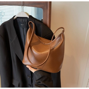 Detailed texture of dark brown pebbled leather on a minimalist bucket hobo shoulder bag