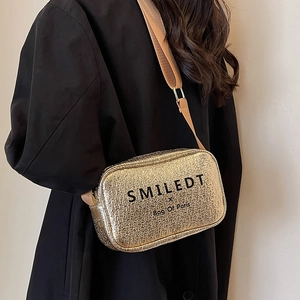 Golden textured crossbody bag with wide strap worn by model over a black coat
