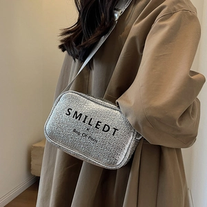 Silver textured crossbody bag with wide strap worn by a model in a brown trench coat