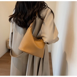 Detailed view of the tan lychee textured leather bucket bag styled with a trench coat