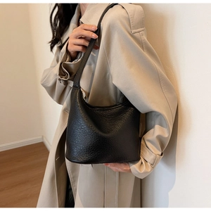 Detail of black pebbled leather hobo bucket bag on model wearing a beige trench coat