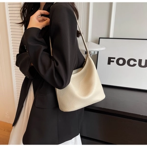 Close-up of beige lychee texture leather hobo bag worn on shoulder by female model