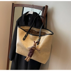 Détail du sac cabas beige clair à motif marbré avec breloque lapin sur un manteau noir