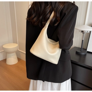 Detail of lychee pattern cream leather hobo bag worn by model in minimalist indoor setting