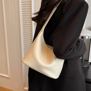 Minimalist beige pebble leather crescent shoulder bag styled on a black blazer jacket
