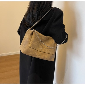 Close-up of the mustard brown suede chain bag worn on a shoulder with a black coat