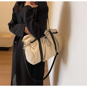 Detailaufnahme einer großen beigen Reisetasche mit schwarzen Riemen an einem Modell