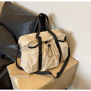 Detail der cremefarbenen Nylon-Reisetasche mit Faltenstruktur und schwarzen Webgurten