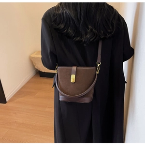 Brown suede bucket bag shown on a model with an adjustable strap and gold clasp
