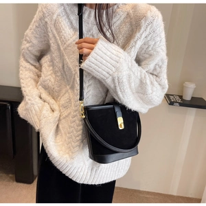 Détail du sac seau noir en daim et cuir avec boucle dorée sur un pull en maille blanc