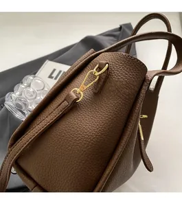 Gros plan du fermoir doré et du cuir grainé lychee sur le sac seau marron foncé