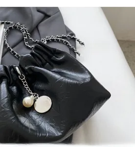 Detail of black crinkle faux leather bucket bag with chain strap and pearl charm