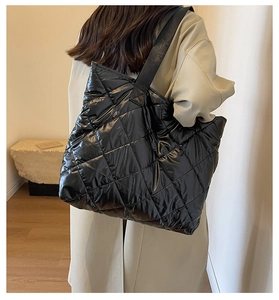 Detail of a large black quilted puffer tote bag with glossy finish and wide strap