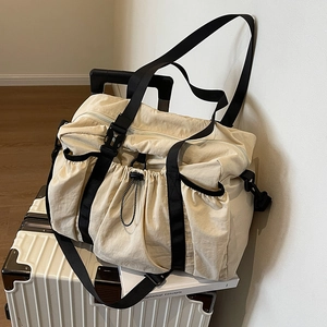 Große beige Reisetasche aus Nylon mit Schnallenriemen auf weißem Koffer