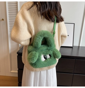 Close-up of green plush crossbody bag with monster eyes on beige sweater