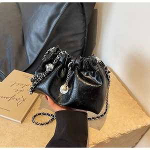 Detail showing black pleated leather bucket bag with silver chain and pearl charm