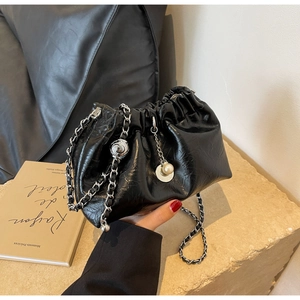 Detail of black pleated cloud bag featuring glossy finish, silver chain, and pearl charms