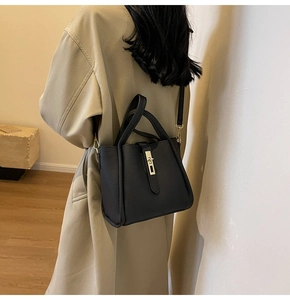Détail d'un sac à main noir en cuir grainé avec fermoir doré porté par un mannequin