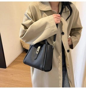 Gros plan d'un sac à main en cuir grainé noir avec boucle dorée sur un trench beige