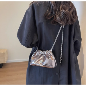 Detail of silver metallic cloud bag with chain strap and bead charm on black coat