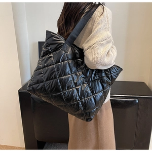 Detail of black quilted tote bag with padded texture and wide shoulder strap