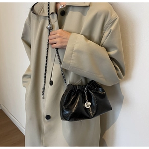 Detail of black pleated cloud bag with elegant chain strap and pearl pendant on model