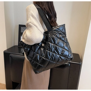 Detail of black quilted tote bag with glossy finish and wide textile shoulder strap