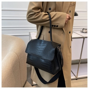 Détail d'un sac noir à motif crocodile avec une large bandoulière amovible réglable