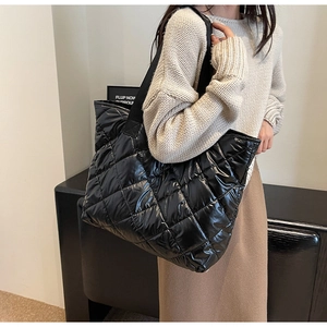 Close-up of black quilted tote bag featuring glossy finish and wide shoulder strap
