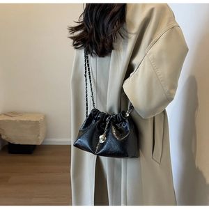 Detail of black pleated bucket bag with chain strap and pearl charm on a model