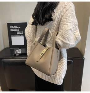 Gros plan d'un sac seau en cuir beige avec fermoir doré sur un mannequin en pull
