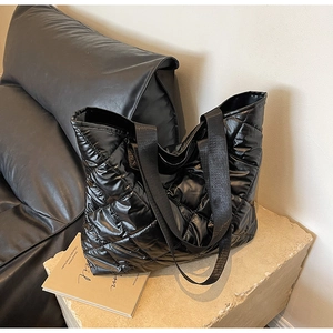 Close-up of black quilted puffer tote bag on stone base showing fabric texture