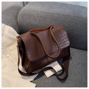 Détail d'un sac cabas marron foncé à texture crocodile et bandoulière tissée sur sofa
