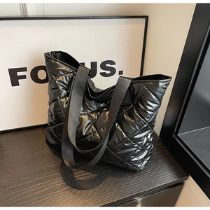 Close-up of black quilted tote bag with glossy finish and wide woven handles on black wood