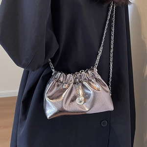 Metallic silver drawstring bucket bag with pearl charm and fine chain strap on dark coat