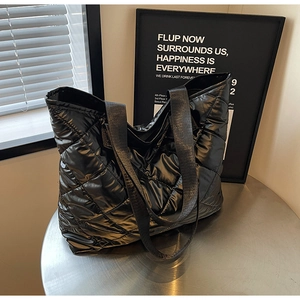 Macro detail of glossy black quilted tote bag showing fine stitching and material texture