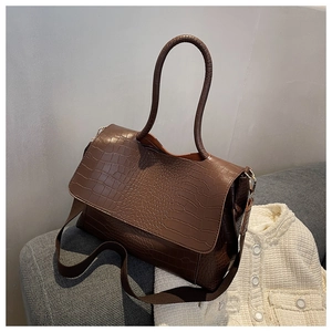 Détail d'un sac à main marron à texture crocodile avec boucles dorées sur canapé