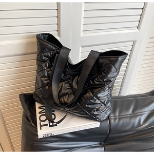 Detailed view of black quilted tote bag with glossy finish and wide woven straps