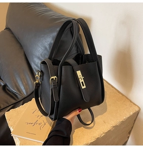 Détail d'un sac seau noir grainé avec fermoir doré sur une surface en pierre
