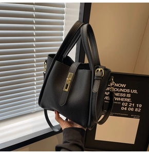 Détail d'un sac à main noir en cuir grainé avec une boucle carrée en métal doré
