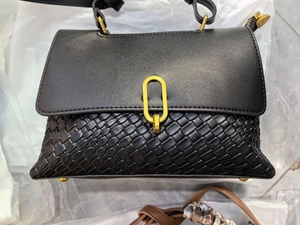 Detailed view of black faux leather handbag featuring a textured woven pattern and gold clasp