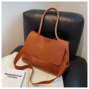 Gros plan du sac marron à motif crocodile avec large bandoulière posé sur un fauteuil