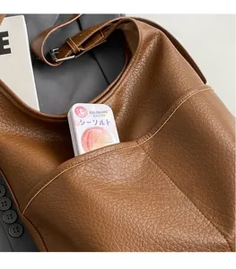 Gros plan sur la texture cuir marron et la bandoulière réglable du sac fourre-tout