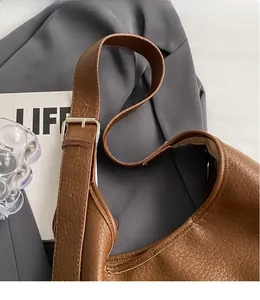 Détail d'un sac en cuir marron grainé avec une large bandoulière réglable et boucle métal