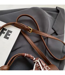 Detail of adjustable shoulder strap and silk scarf wrapped handle on brown leather bag