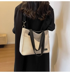 Detail of canvas tote bag with contrast black straps and brand label on dark coat