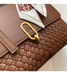Detail view of brown woven leather bag with gold buckle and white printed scarf wrap
