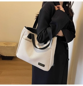 Detailed side view of a large canvas tote bag with contrast black straps and brand tag